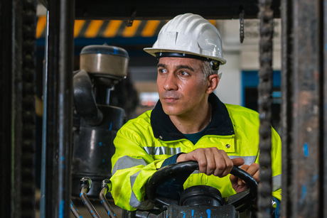 Man wear safety helmet happy smiling looking at camera driver forklift warehouse in factory. Male worker industrial operate. control loading container box. logistics export import concept.