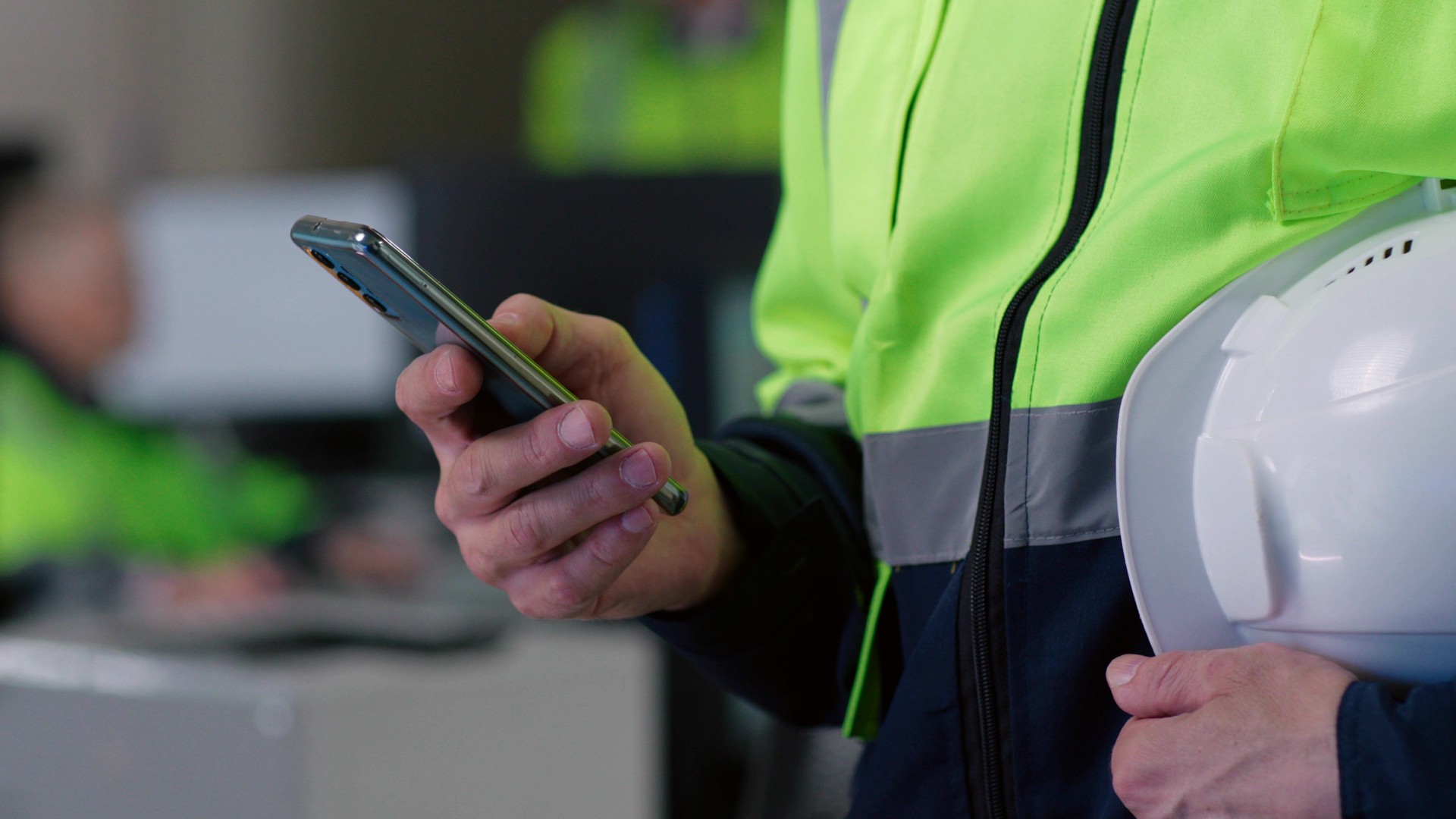 Cropped shot of builder chat on smartphone holding hardhat. Close up of engineer in safety uniform using cellphone