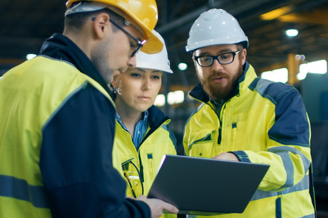 Three Industrial Engineers Talk with Factory Worker while Using Laptop. They Work at the Heavy Industry Manufacturing Facility.