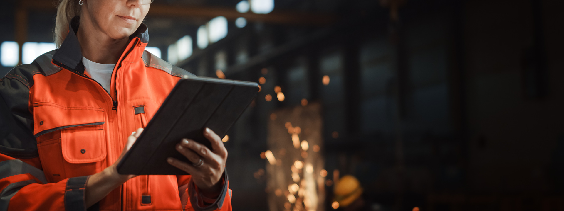 Professional Heavy Industry Engineer Worker Wearing Safety Uniform and Hard Hat Uses Tablet Computer. Serious Successful Female Industrial Specialist Standing in a Metal Manufacture Warehouse.