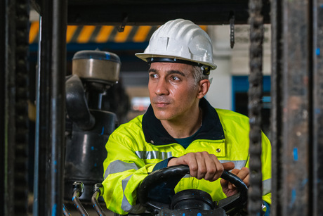 Man wear safety helmet happy smiling looking at camera driver forklift warehouse in factory. Male worker industrial operate. control loading container box. logistics export import concept.