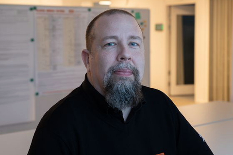 Patrick Callhammar sitter på en stol framför ett skrivbord och i bakgrunden syns en whiteboard och korridor