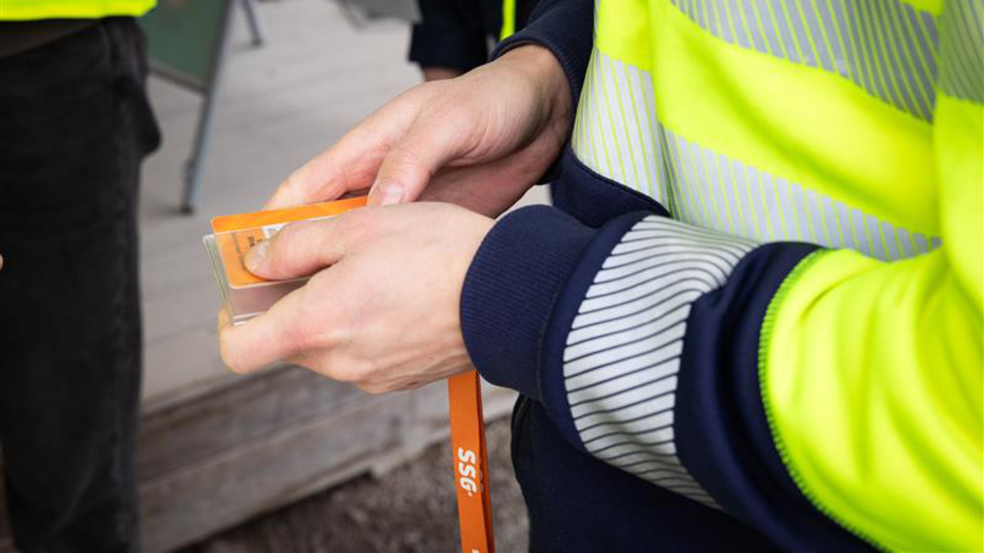 Händer som sätter in sitt orangea SSG-kort i en korthållare med tillhörande SSG-rem att sätta över halsen