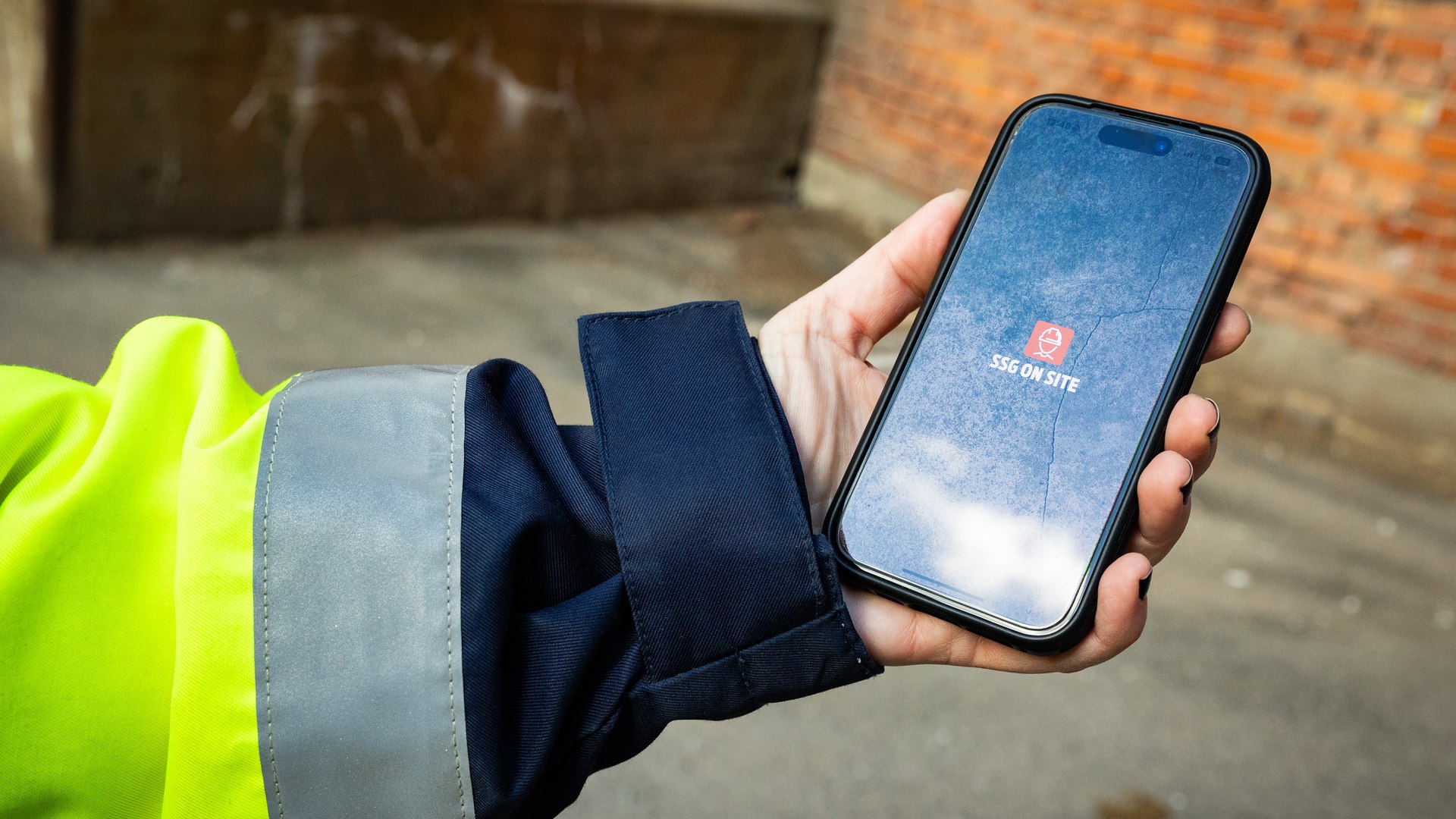 en hand som håller i en telefon där det står SSG ON SITE och en symbol av en person i hjälm